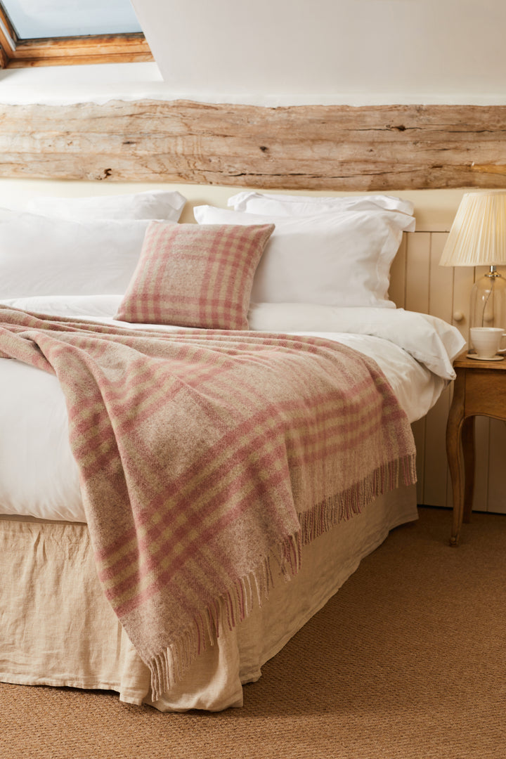 Tweedmill Dusky Pink Check Wool Throw elegantly draped over a king-size bed with a matching cushion.