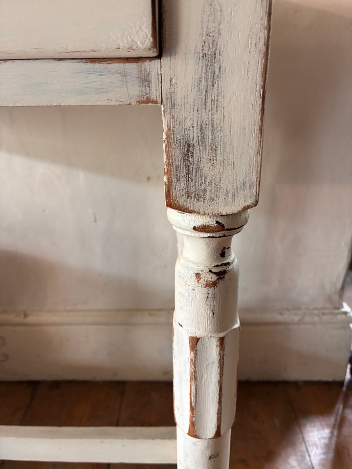 Close-up of a vintage painted side table leg showcasing distressed white finish and elegant turned design.