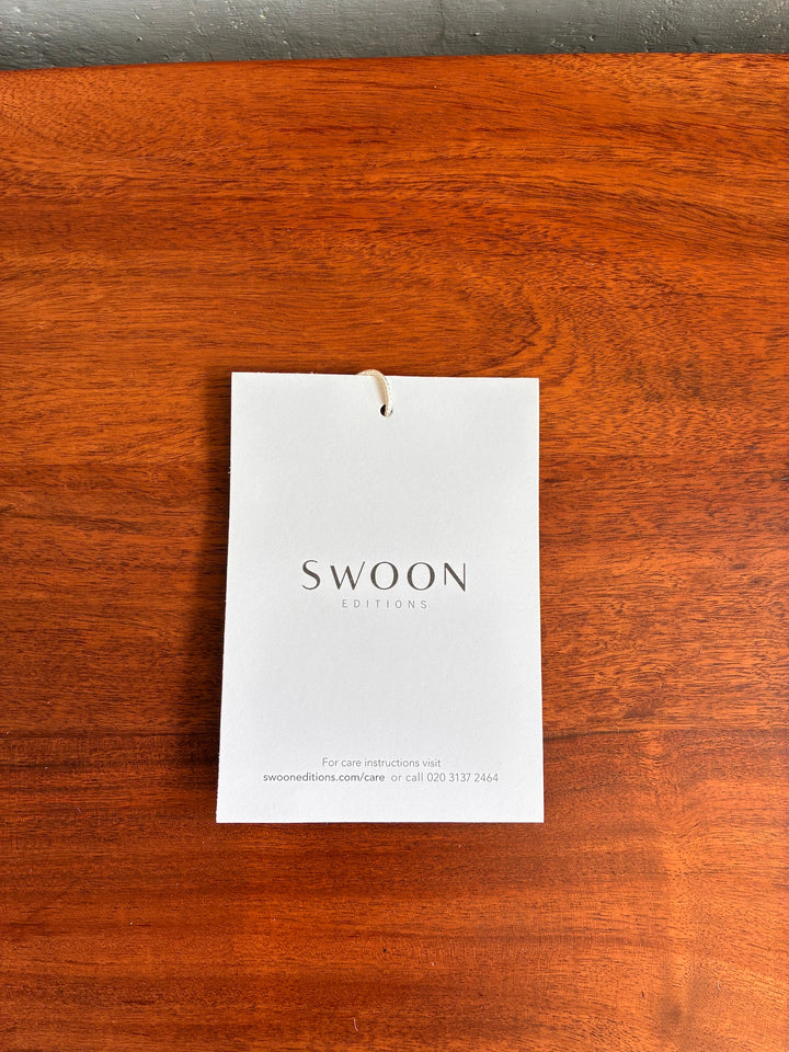 Swoon Editions care instruction tag on a Retro Swoon TV Stand's rich wooden surface.