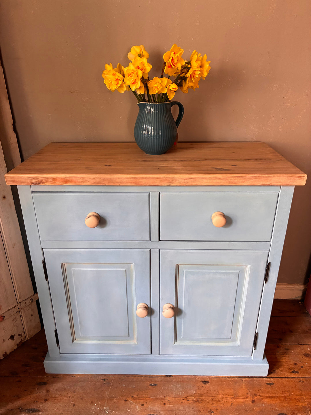 A simple pine cupboard painted in Annie Sloan Louis Blue styled with a blue jug filled with daffodils at Source for the Goose, Devon