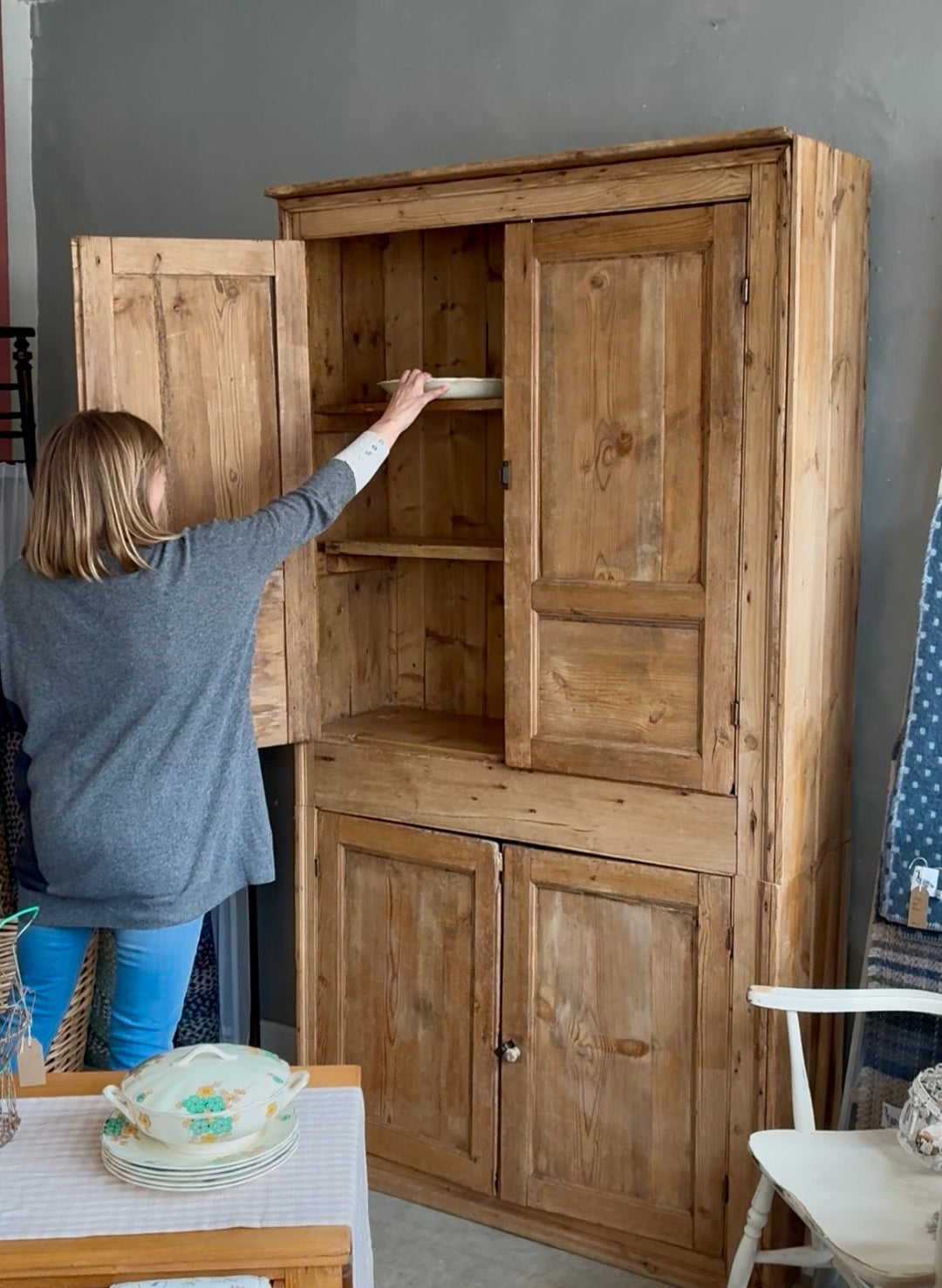 Jill, owner of Source for the Goose in Devon, placing plates in a rustic pine cupboard