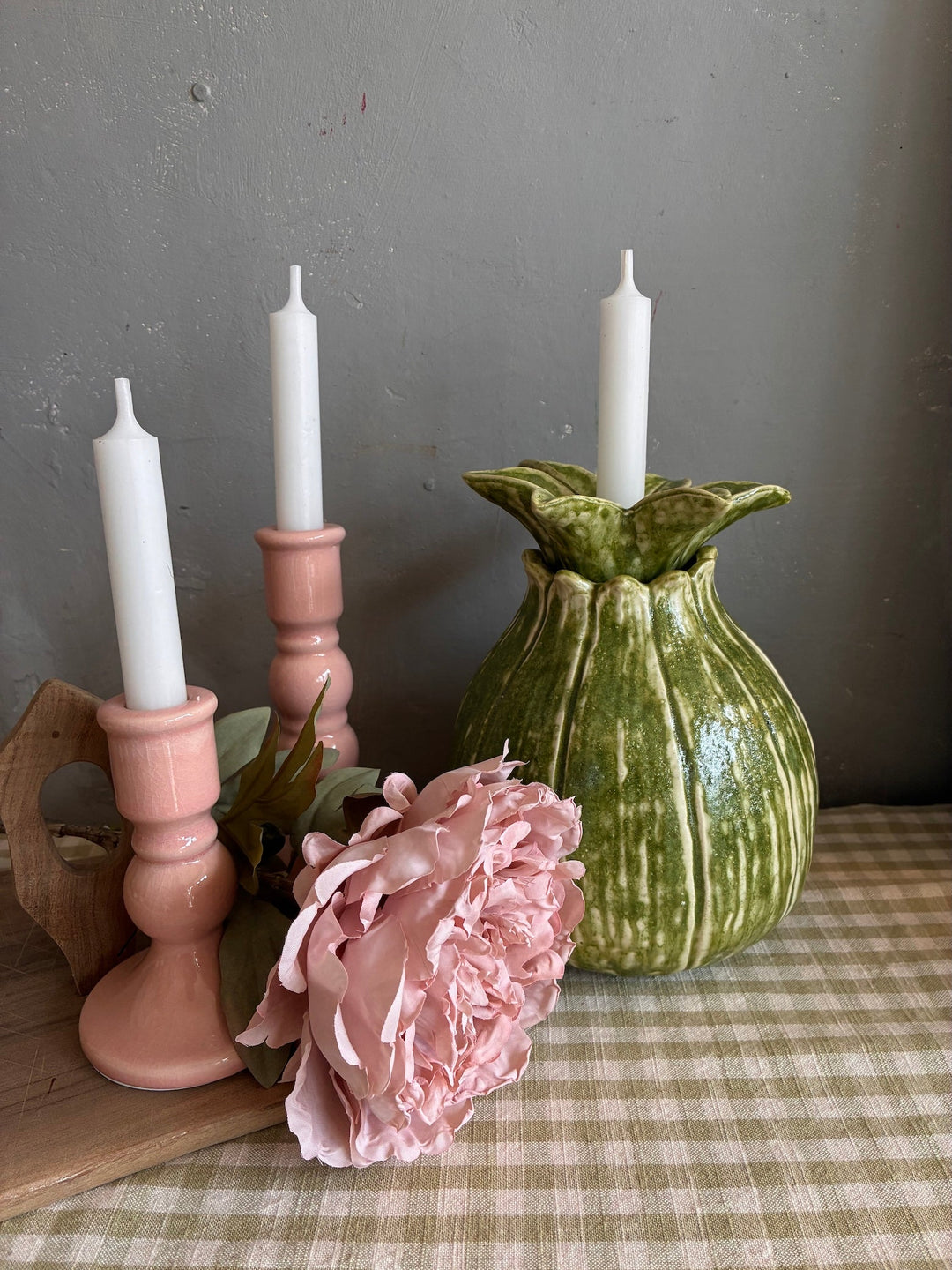 two pink candlesticks with white candles, beside a green ceramic vase/candleholder with a pretty faux peony standing on a green gingham table runner at Source for the Goose, Devon