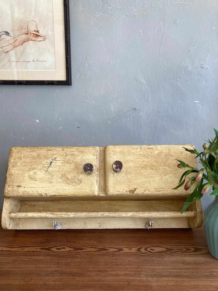 1930s wooden wall cupboard with towel rail in muted ochre finish, featuring hooks and floral decor, Source for the Goose, Devon.