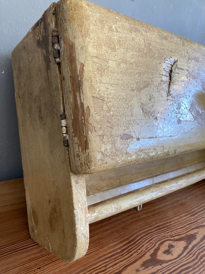 Close-up of a vintage 1930s wooden wall cupboard with worn ochre paint and towel rail details from Source for the Goose, Devon.