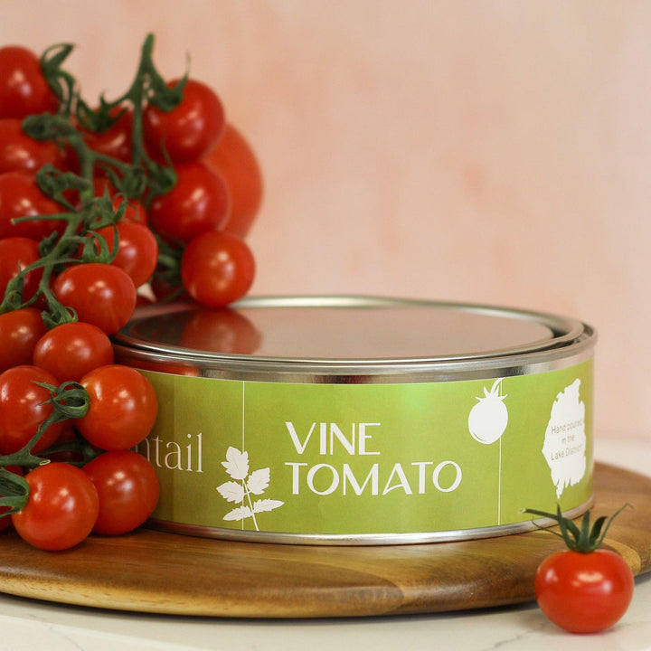 Pintail Candles Vine Tomato triple wick candle surrounded by fresh cherry tomatoes on a wooden surface.