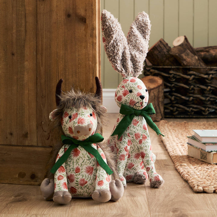 Hattie Hare Door Stop - Floral Design and a floral cow plush sitting on the floor next to a wooden wall.