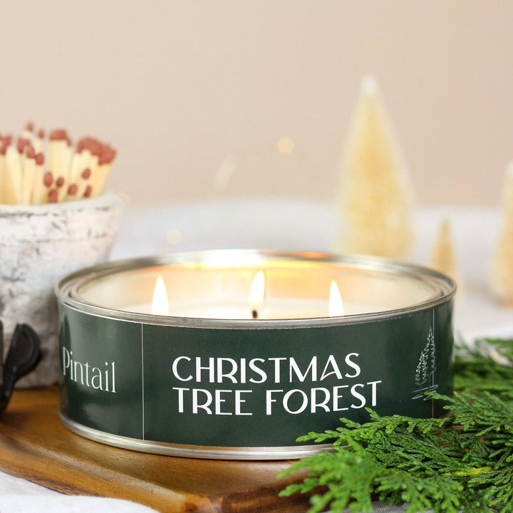 Pintail Christmas Tree Forest Triple Wick candle surrounded by evergreen and decorative holiday elements.