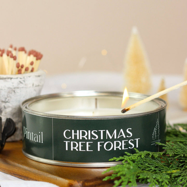 Pintail Christmas Tree Forest Triple Wick Candle with a match being lit, surrounded by festive decor.