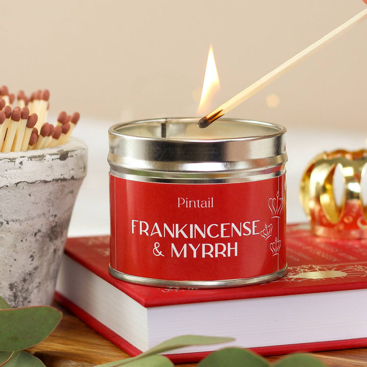 Pintail Candles Frankincense & Myrrh in Classic Tin, lit with a match, surrounded by festive decor, Source for the Goose Devon.