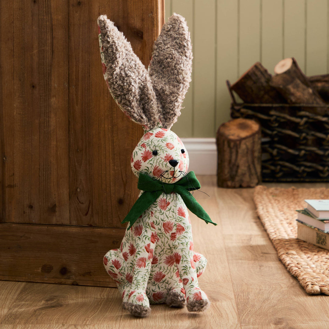 Hattie Hare Door Stop - Floral Design with handpainted floral patterns and green bow in a rustic setting.