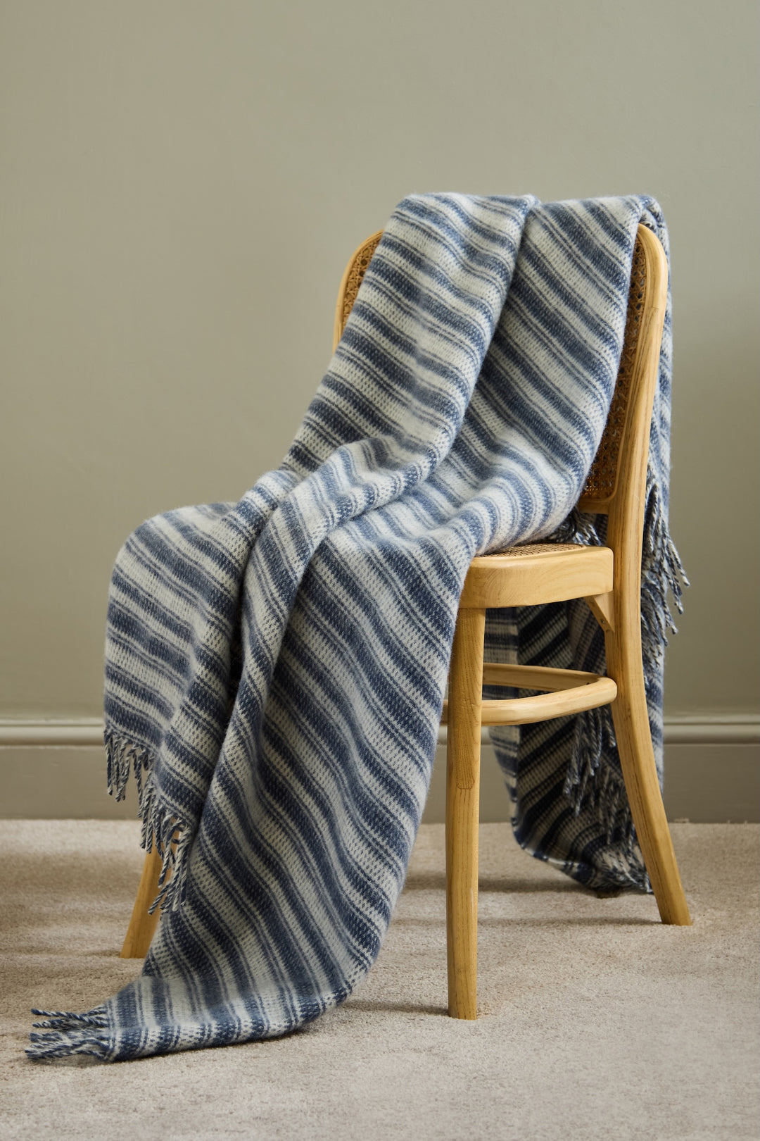 Tweedmill Blue Slate Wool Throw - Aber Stripe draped over a wooden chair, featuring blue stripes and tassels.