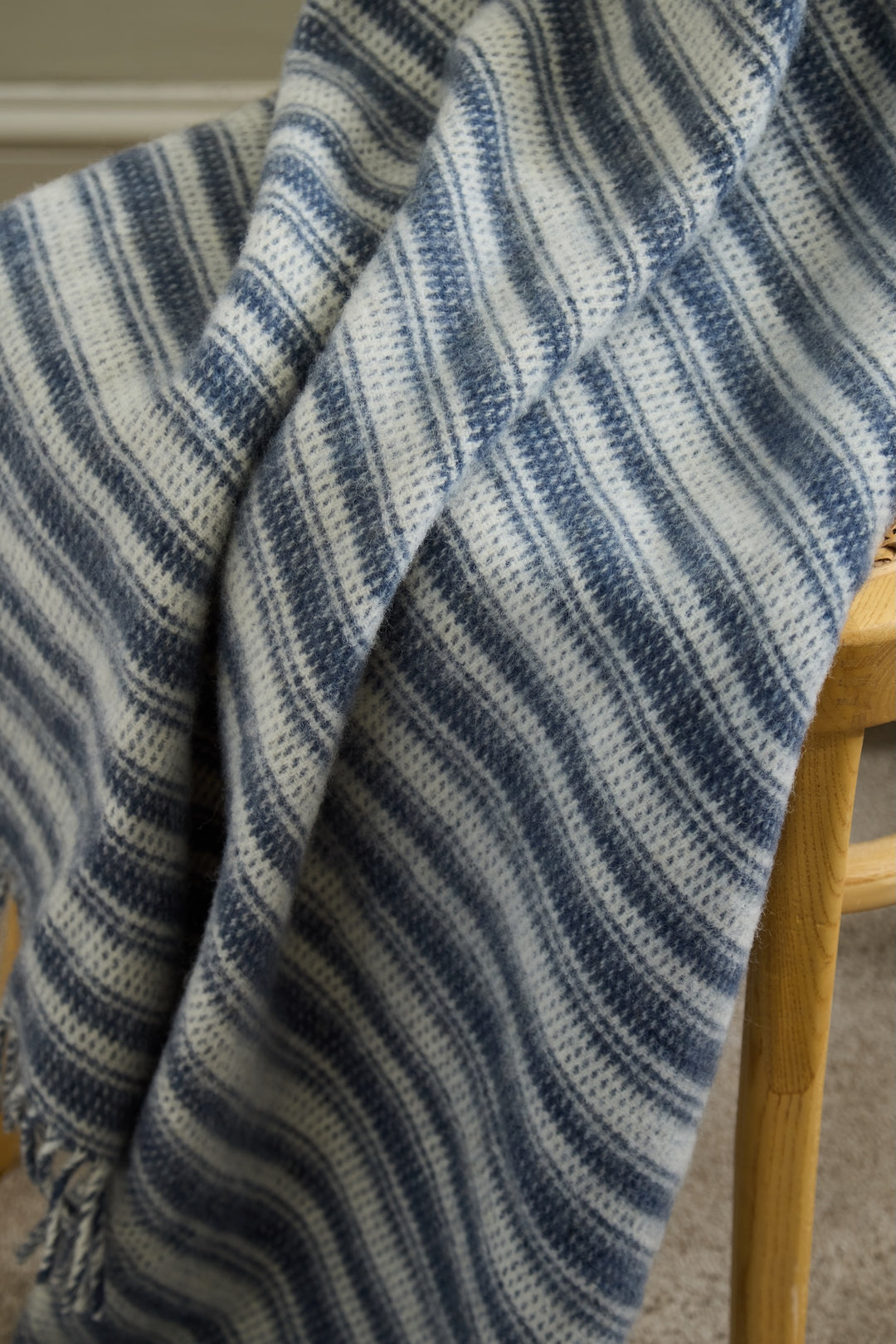 Tweedmill Blue Slate Wool Throw - Aber Stripe draped over a chair with stylish blue stripes and tassels, perfect for cosy throws.