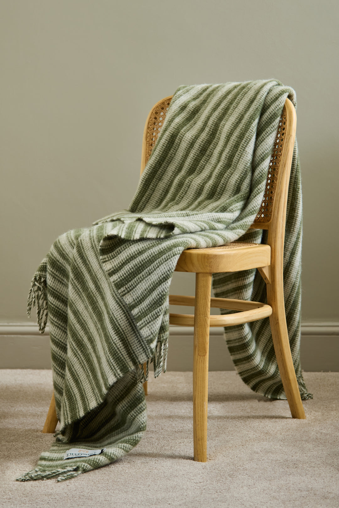 Tweedmill Olive Green Aber Stripe Wool Blanket draped over a wooden chair in a cozy indoor setting.