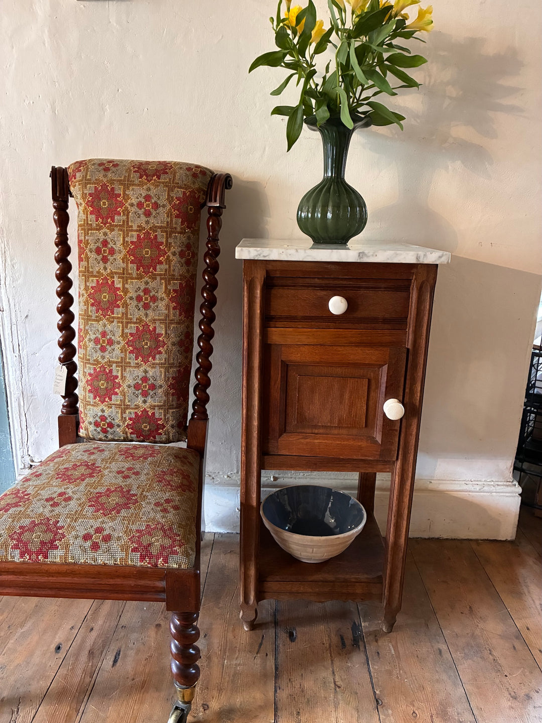French Antique Oak Bedside Table with marble top beside an upholstered chair and vase of flowers.