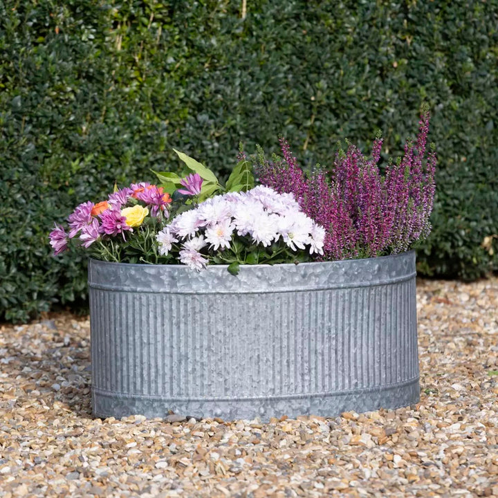 Oval Ribbed Zinc Planter filled with colorful flowers, showcasing its rustic charm and weather-resistant design.