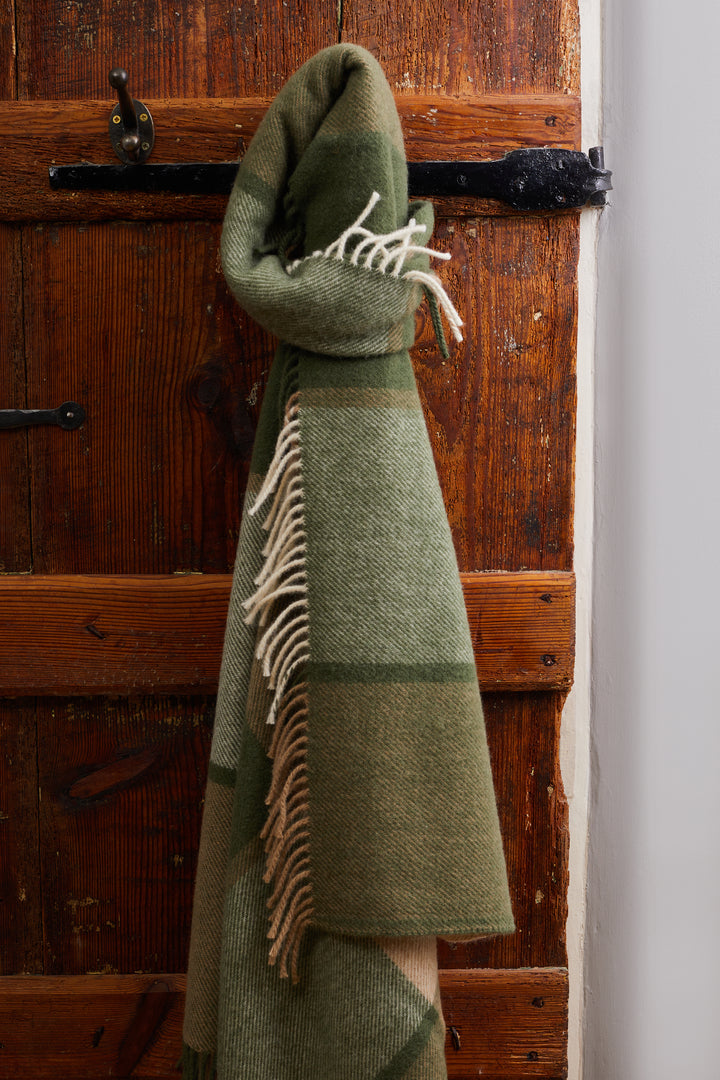 Tweedmill Block Check Olive Throw - Pure Wool hanging against a wooden door, showcasing its cosy home appeal.