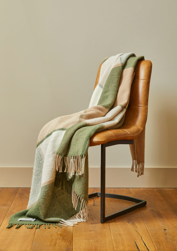 Tweedmill Block Check Olive Throw - Pure Wool draped over a chair, showcasing its cosy home appeal and lovely green tones.