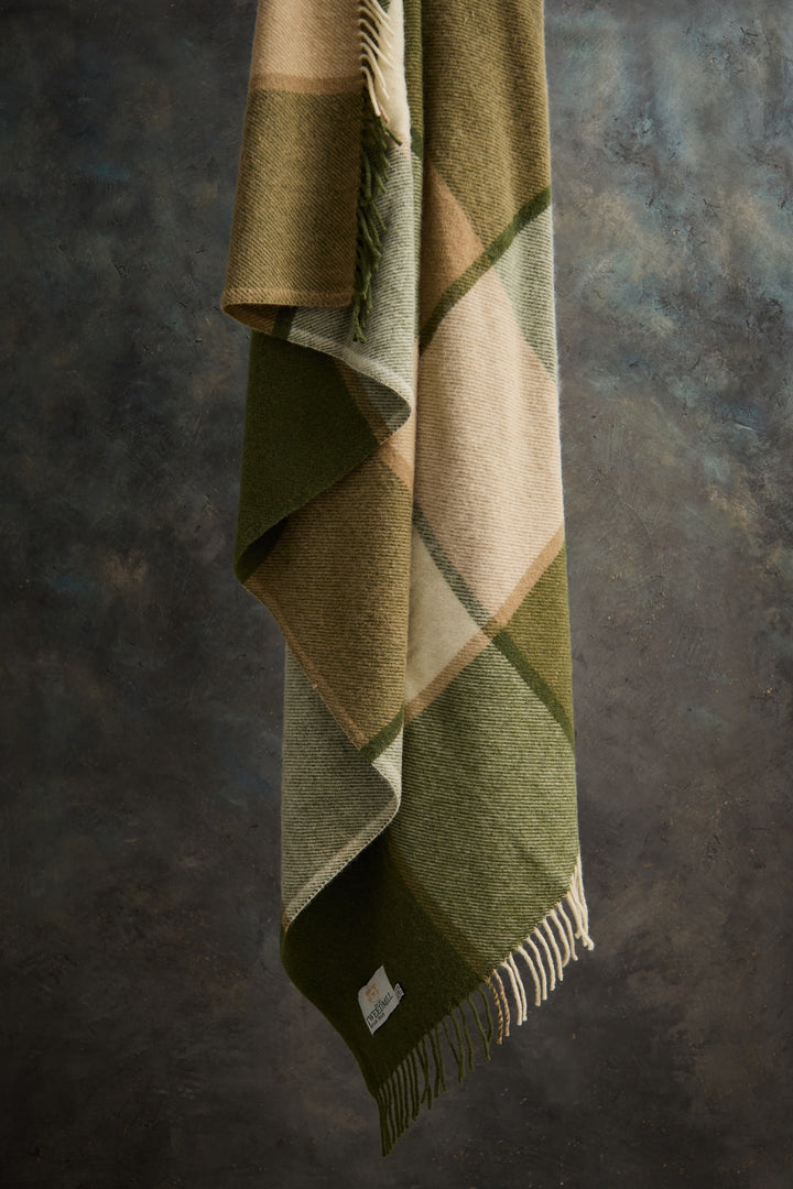Tweedmill Block Check Olive Throw - Pure Wool hanging elegantly, showcasing its earthy tones and tassels for a cosy home.