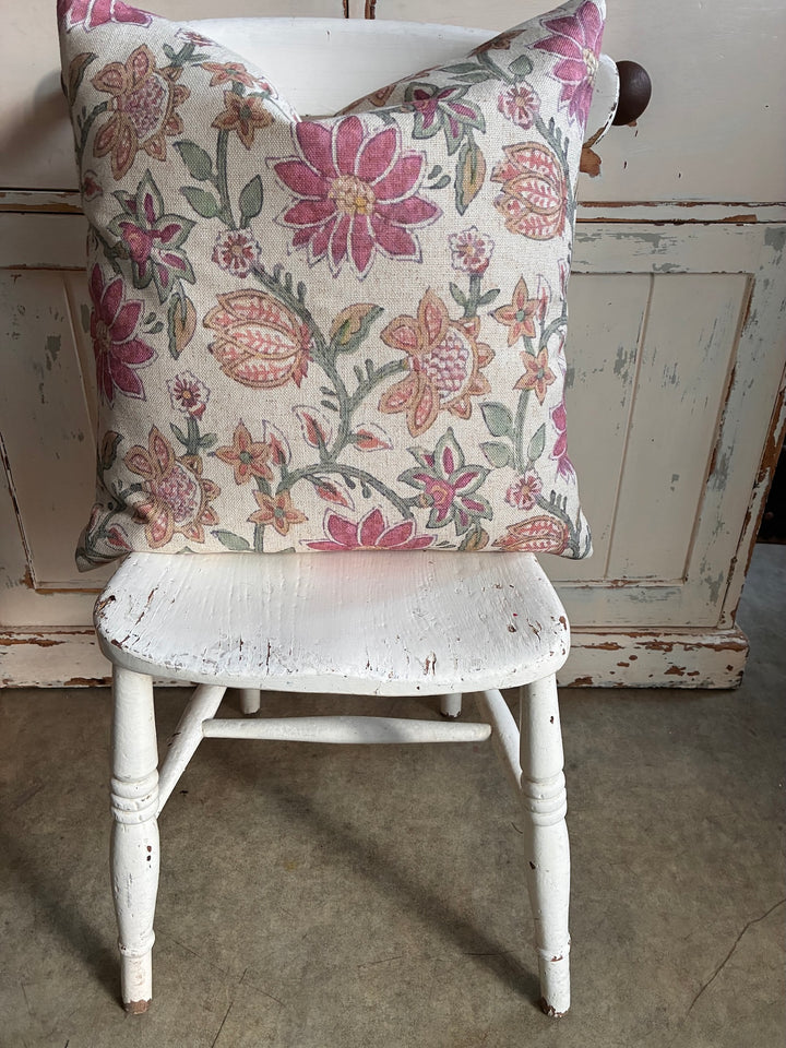 Floral-patterned cushion on a white wooden chair against a rustic wooden wall.