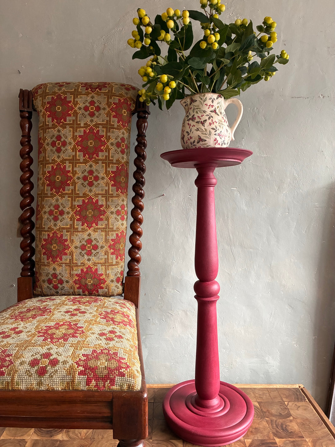 Burgundy Vintage  Wooden Plant Stand showcasing a bouquet in a floral jug beside a patterned chair.