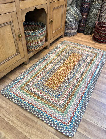 Colorful braided rug on a wooden floor with a wooden cabinet and baskets in the background.