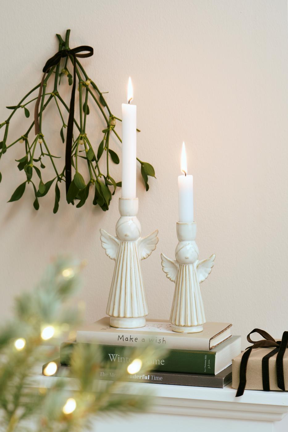 Festive ceramic angel candleholders on stacked books, featuring elegant angel designs and glowing candles, by Source for the Goose, Devon.