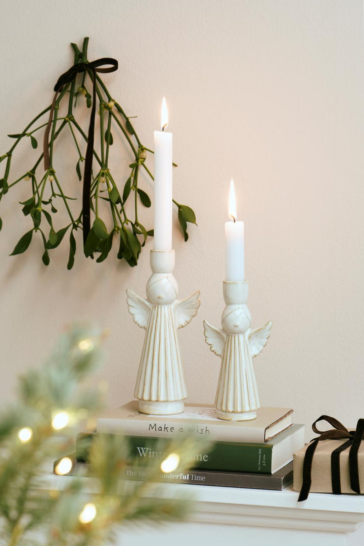 Festive ceramic angel candleholders on stacked books, featuring elegant angel designs and glowing candles, by Source for the Goose, Devon.