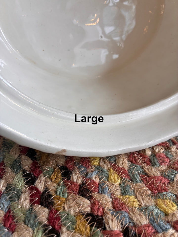 Large white ceramic bowl with a smooth finish on a textured multi-colored woven surface.