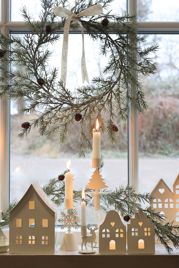 Festive Christmas window display with wreath, candles, and decorative houses, creating a warm holiday ambiance.