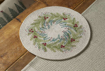 Circular Christmas wreath placemat on wood table, featuring festive design with greenery and berries, from Source for the Goose Devon.
