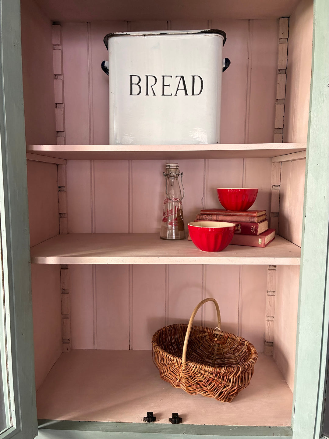 Duck Egg Blue Glazed Kitchen Dresser with a white bread tin, red bowls, and a woven basket on pale pink shelves.