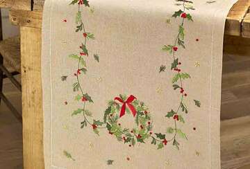 Embroidered Christmas Wreath Table Runner - Natural featuring holly and wreath design on wooden table.