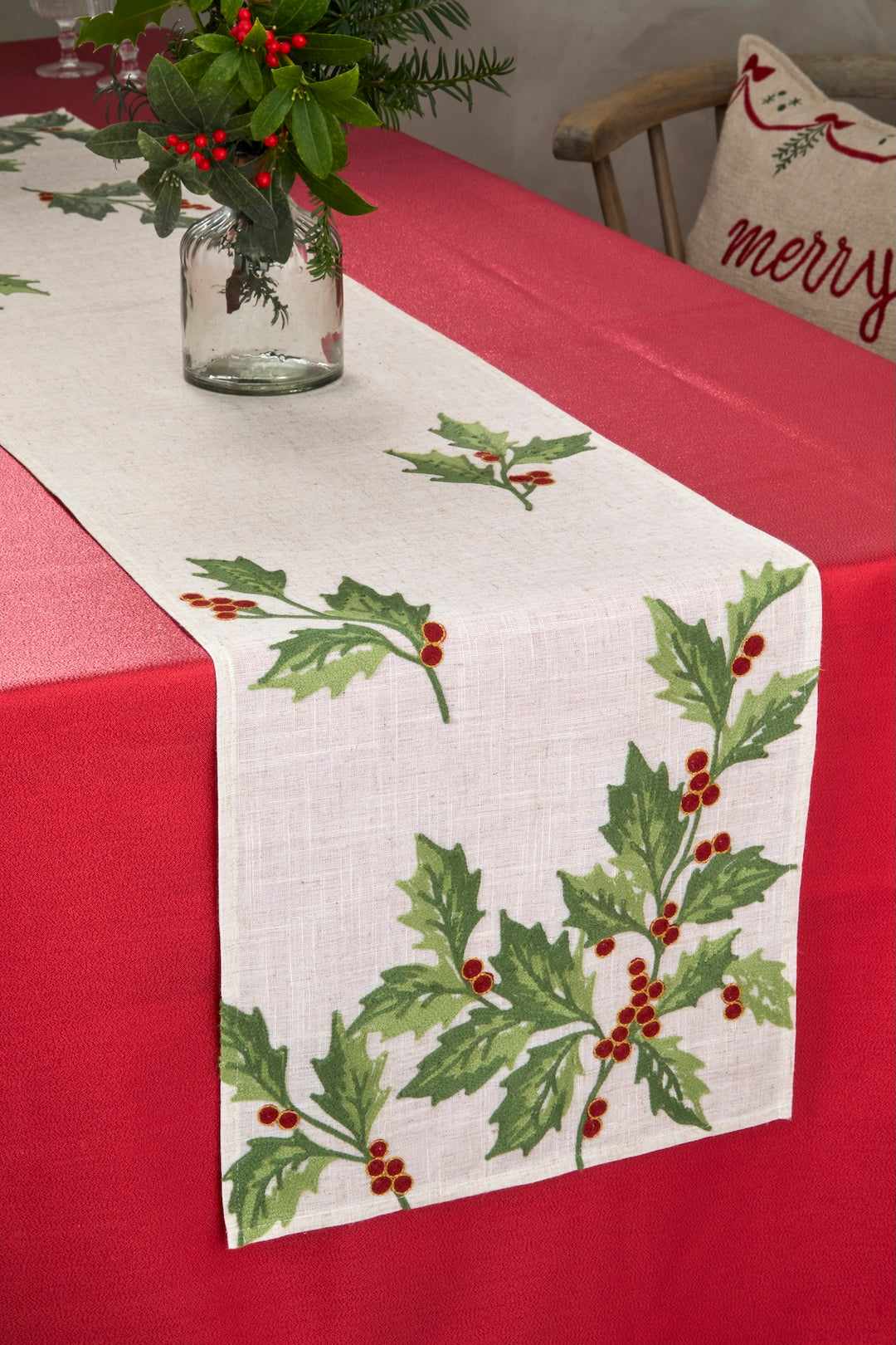 Embroidered Festive Holly Berry Table Runner on a festive dining table with red tablecloth and greenery centerpiece.