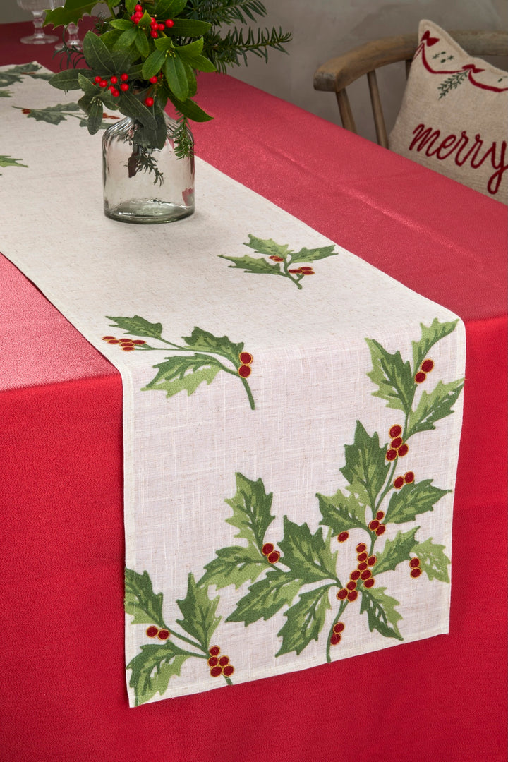 Embroidered Festive Holly Berry Table Runner on a festive dining table with red tablecloth and greenery centerpiece.