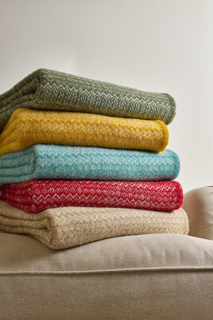 Stack of colorful blankets including the Tweedmill Oatmeal Fair Isle Wool Throw on a sofa.