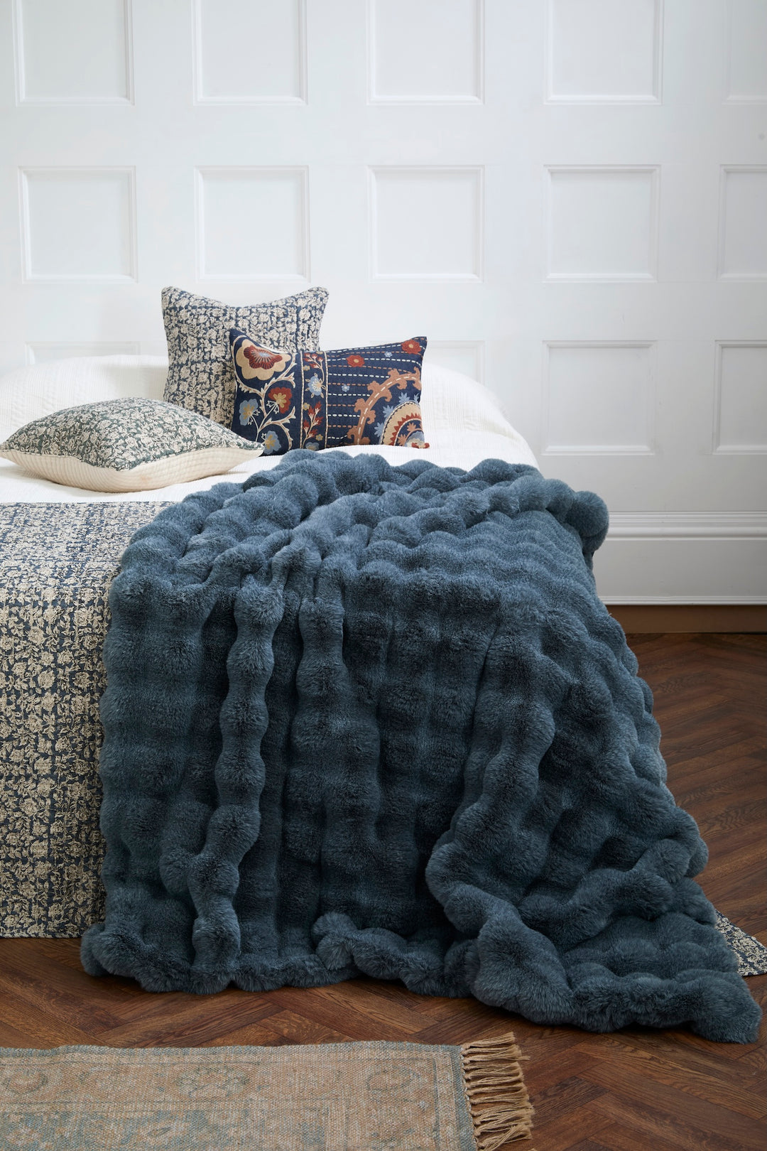 Slate Blue Faux Fur Throw draped over a bed with decorative pillows, showcasing its luxurious texture.