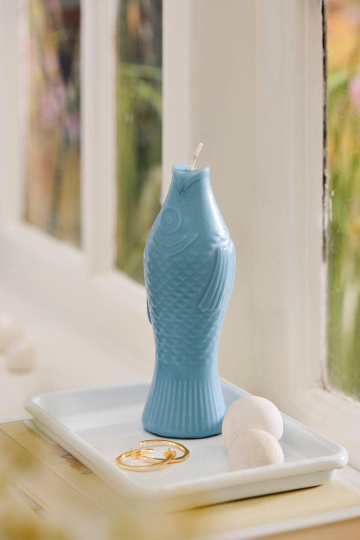 Quirky fish-shaped dusty blue candle on a tray, adding playful charm to home decor. Source for the Goose, Devon.