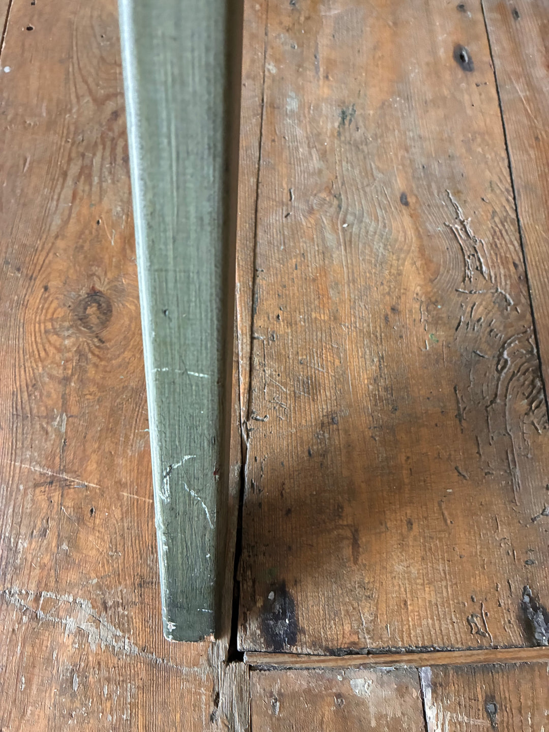 Detail of the edge of a Folding Butlers Tray Desk Table in olive green paint on wooden floor.