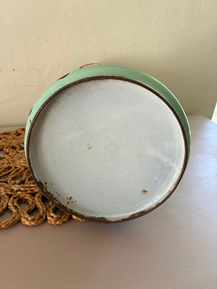 Bottom view of a vintage Art Nouveau French enamel bowl highlighting its pastel green edge and aged patina.