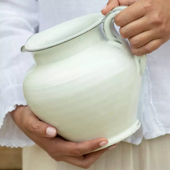 Holding a short handmade ceramic jug with vintage style, featuring a flawless white glaze, perfect for rustic home decor and versatile uses