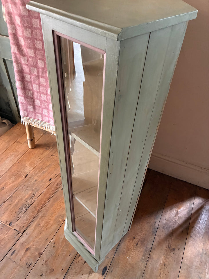 Soft Green Corner Display Cabinet with glass door, pink-edged trims, and two shelves for showcasing decor.