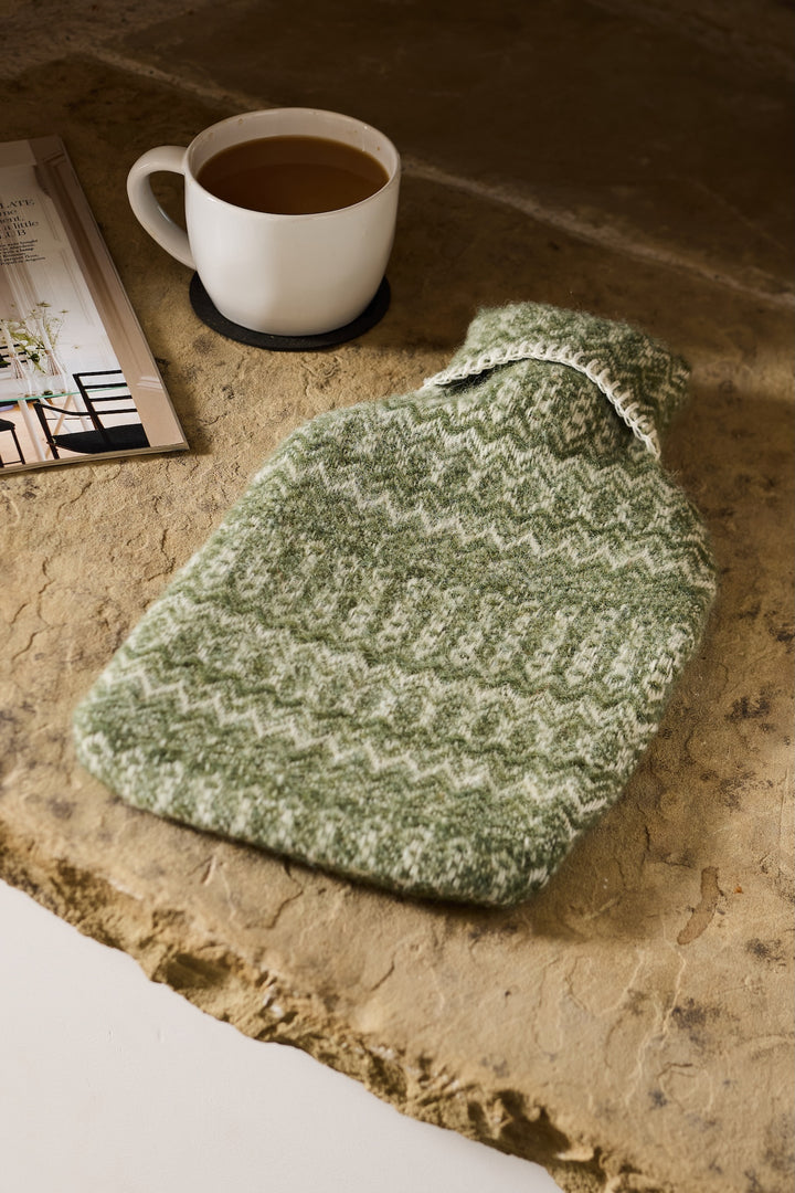 Fair Isle Wool Hot Water Bottle - Two Colours on a stone surface with a cup of tea and magazine, perfect for a cosy home.