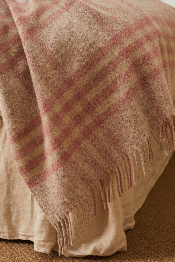 Tweedmill Dusky Pink Check Wool Throw draped over a king-size bed, showcasing pink check pattern and tassels.