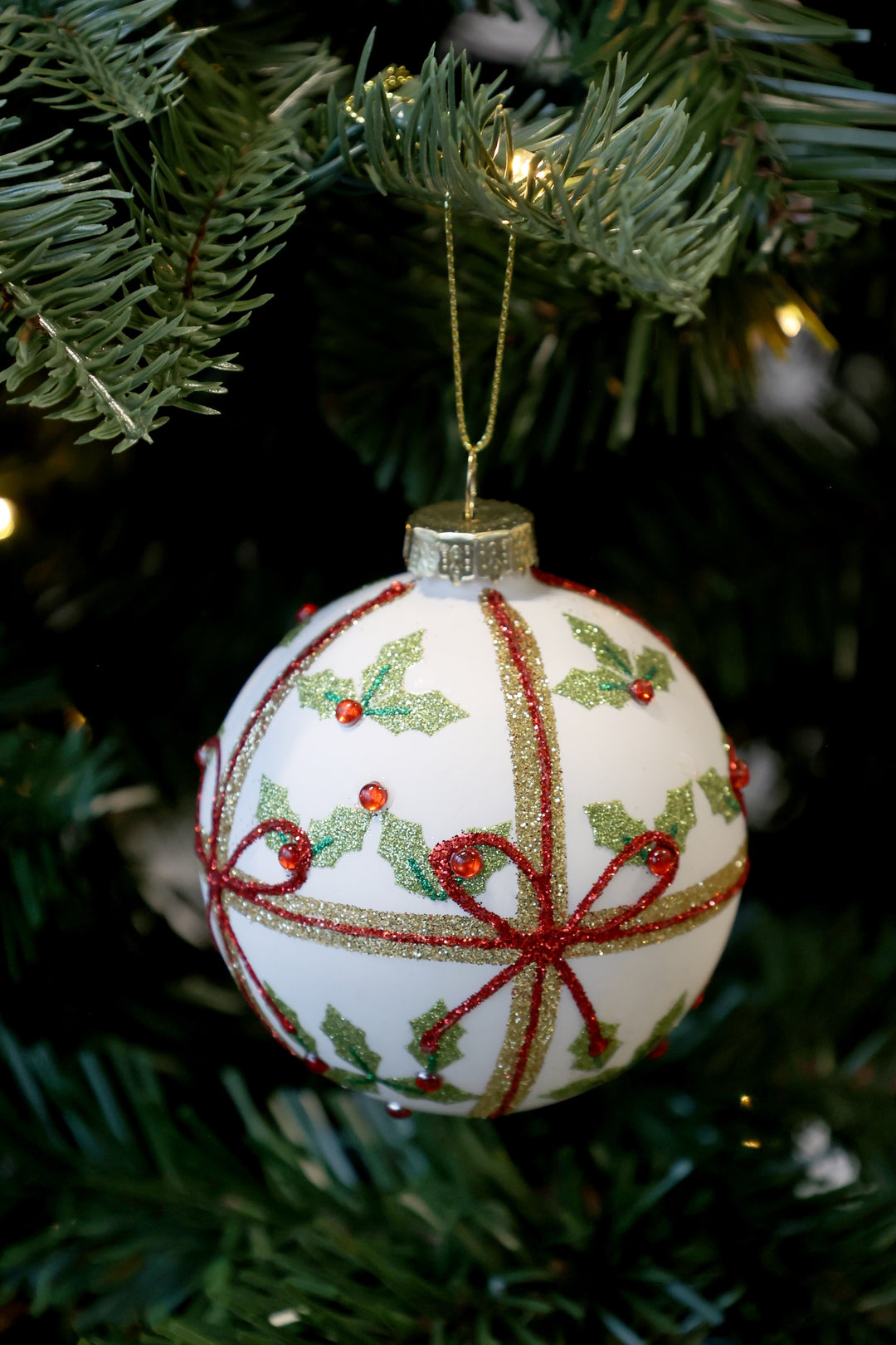 Holly and Bows glass Christmas bauble hanging on a tree, featuring festive design by Source for the Goose, Devon.
