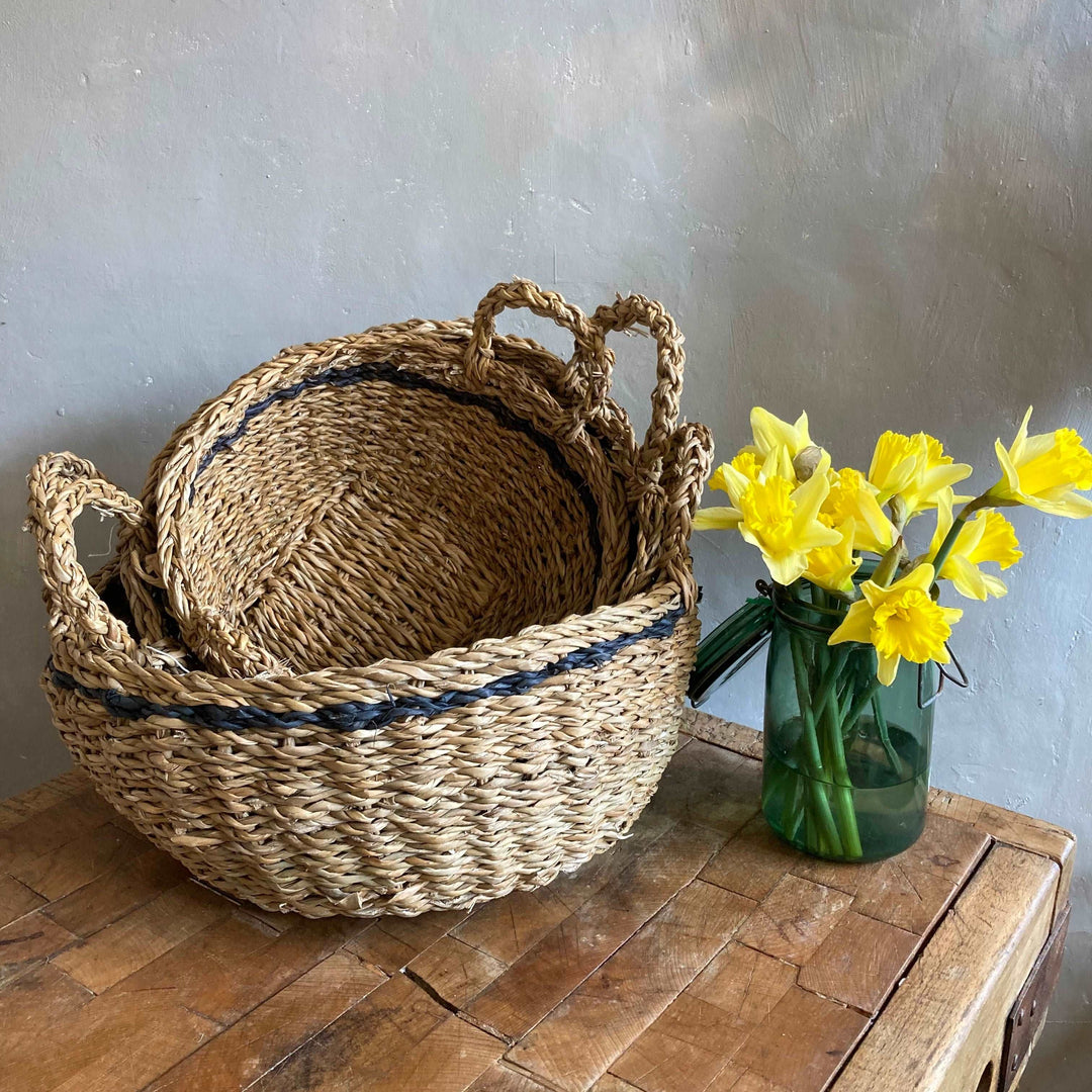 Round Stripe Hogla Basket on table with vintage glass jar filled with daffodils