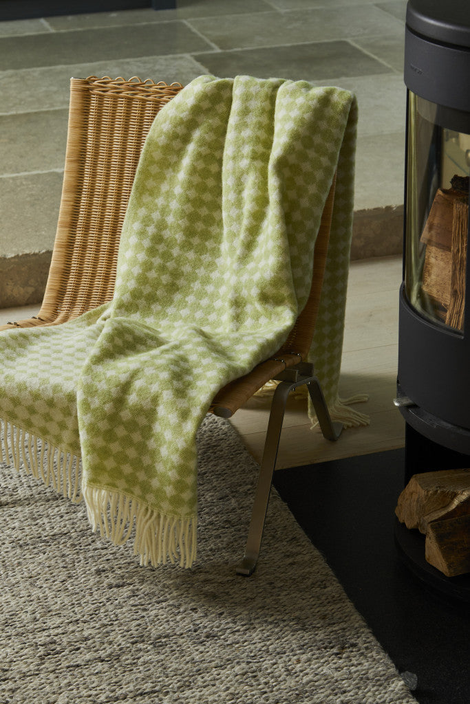 Tweedmill Jacquard Spot Sage Green Wool Blanket draped on a chair, showcasing cream spots and elegant tassels.