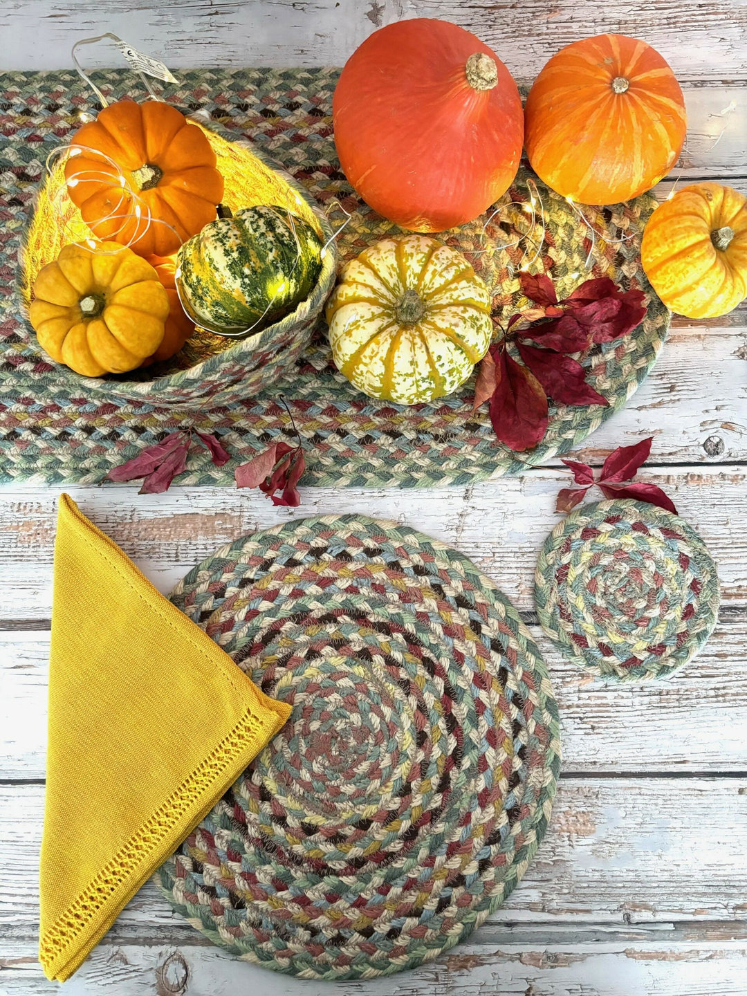 Colorful jute table settings with pumpkins and autumn leaves on a rustic wood table for a cozy dining experience.