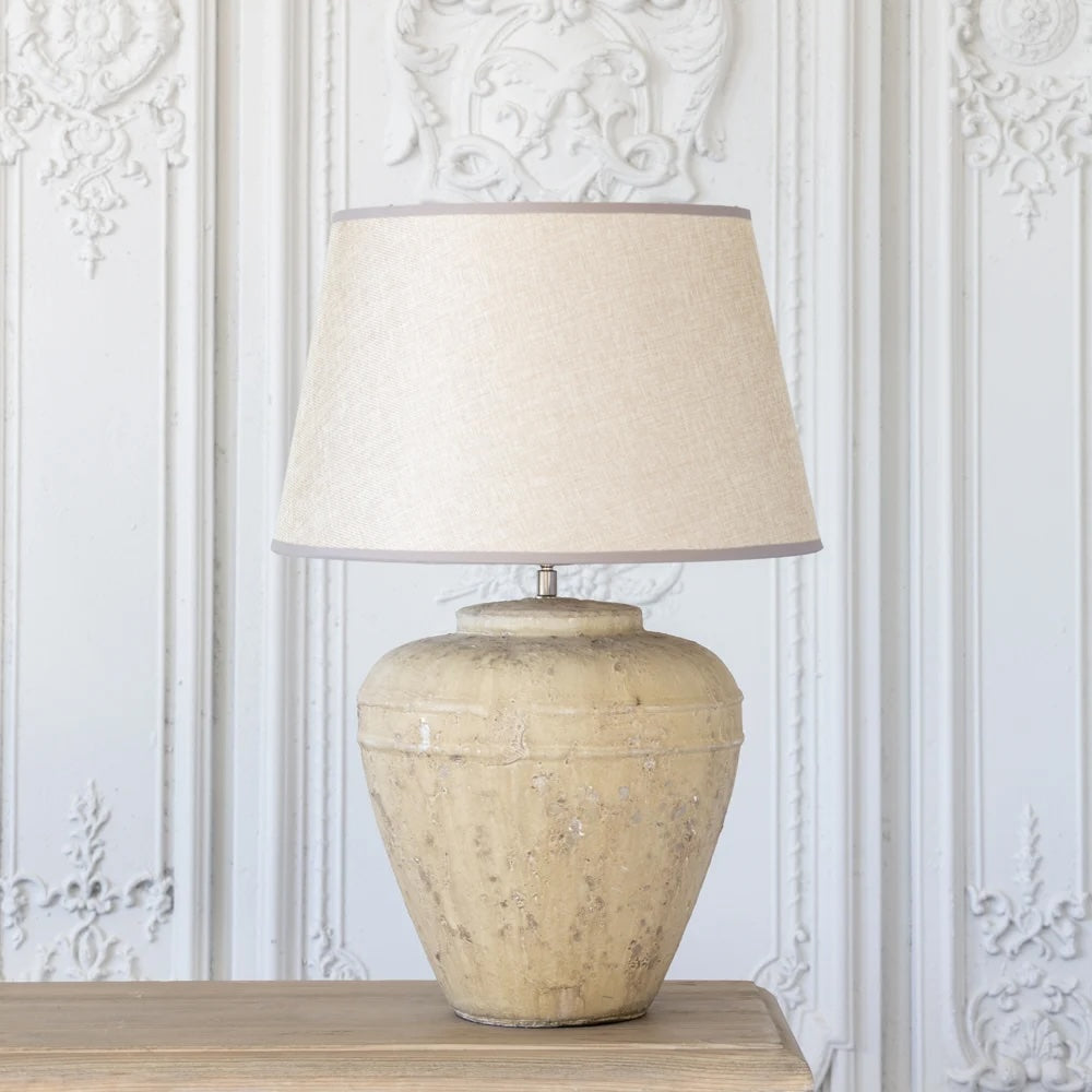 Marius Lamp - Stoneware Base With Woven Linen Shade on a wooden table against a textured white backdrop.