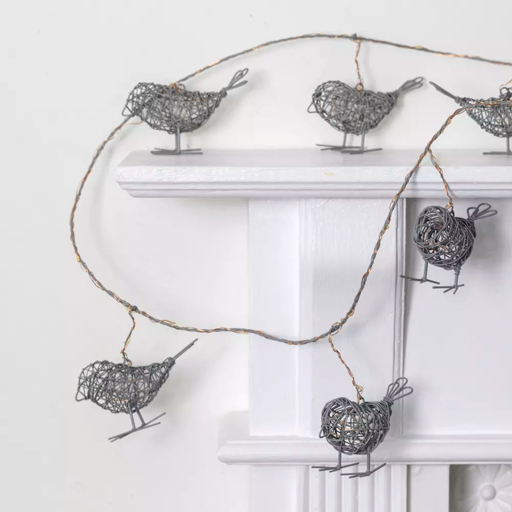 Light Up Wire Bird Garland - Antique Grey draped over a mantel with intricately crafted wire birds illuminated by LED lights.