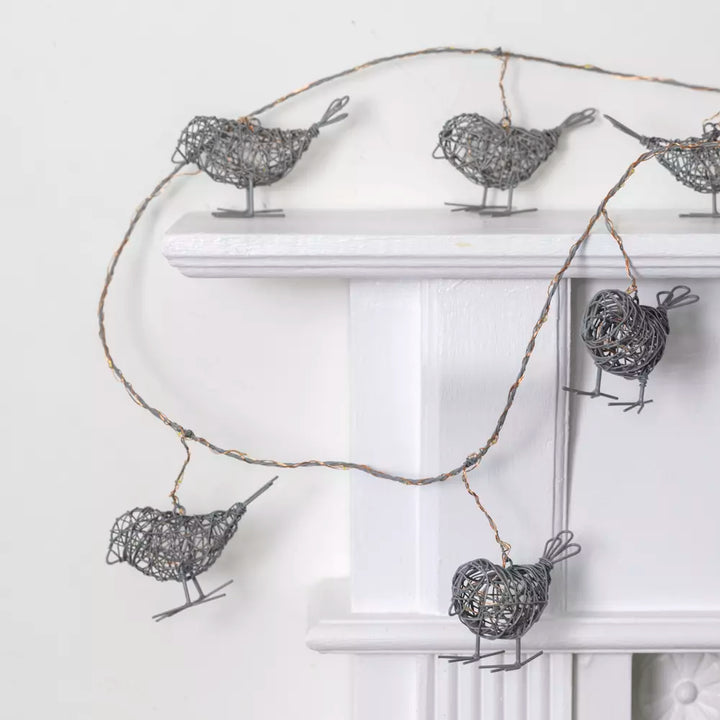 Light Up Wire Bird Garland - Antique Grey draped over a mantel with intricately crafted wire birds illuminated by LED lights.